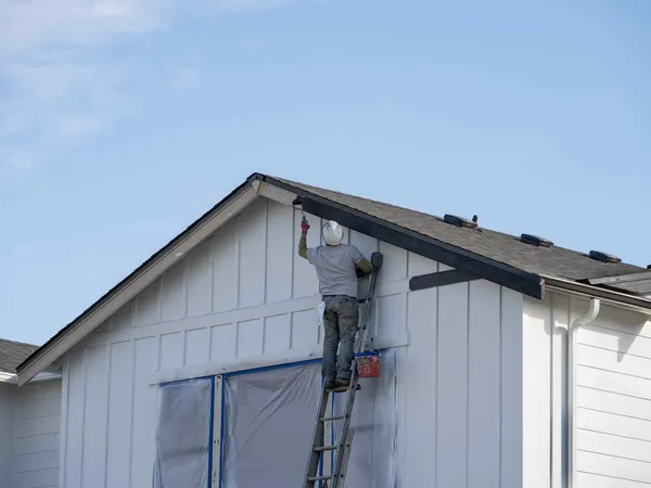 A painter on a ladder cutting in fascia trim, with the window below masked off
