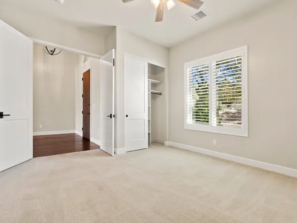 An empty freshly painted bedroom with white trim, plantation shutters and a closet