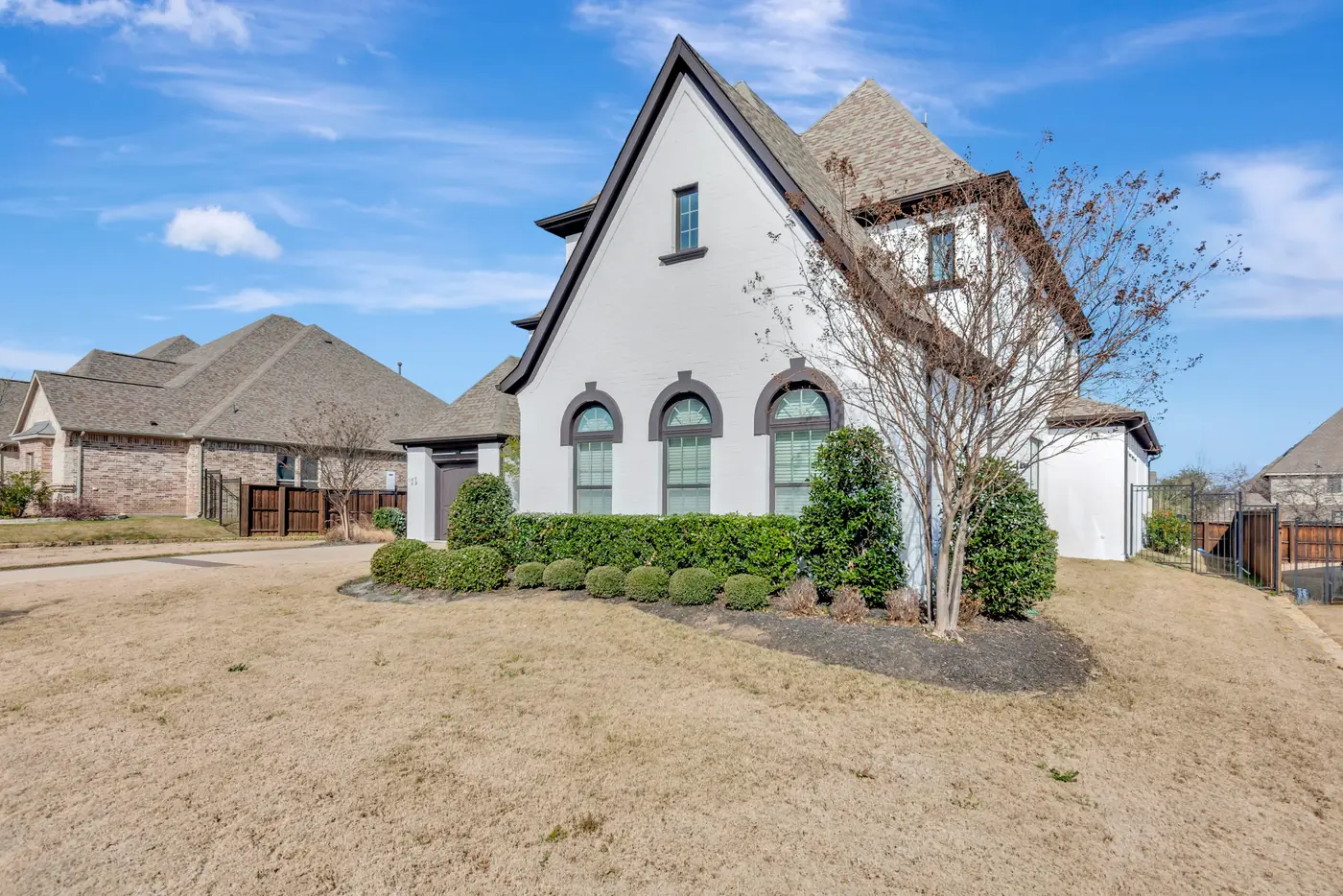 Gable end of a white painted brick home with three arched windows and a bare crepe myrtle in the foreground