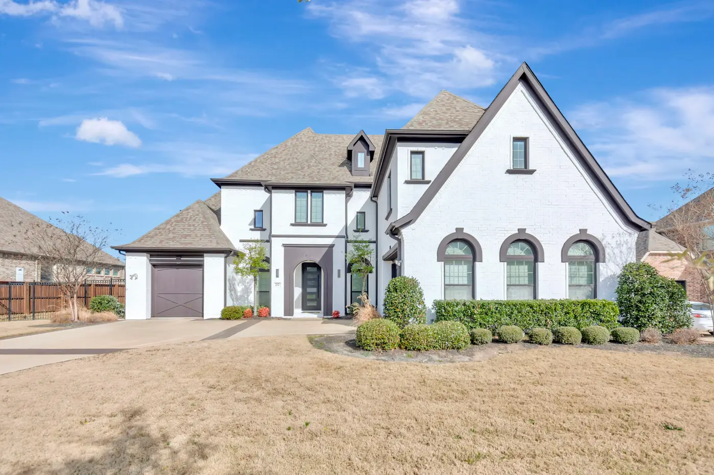 Three-quarter view of a repainted white brick home with dark trim, an arched entry and clipped box hedging