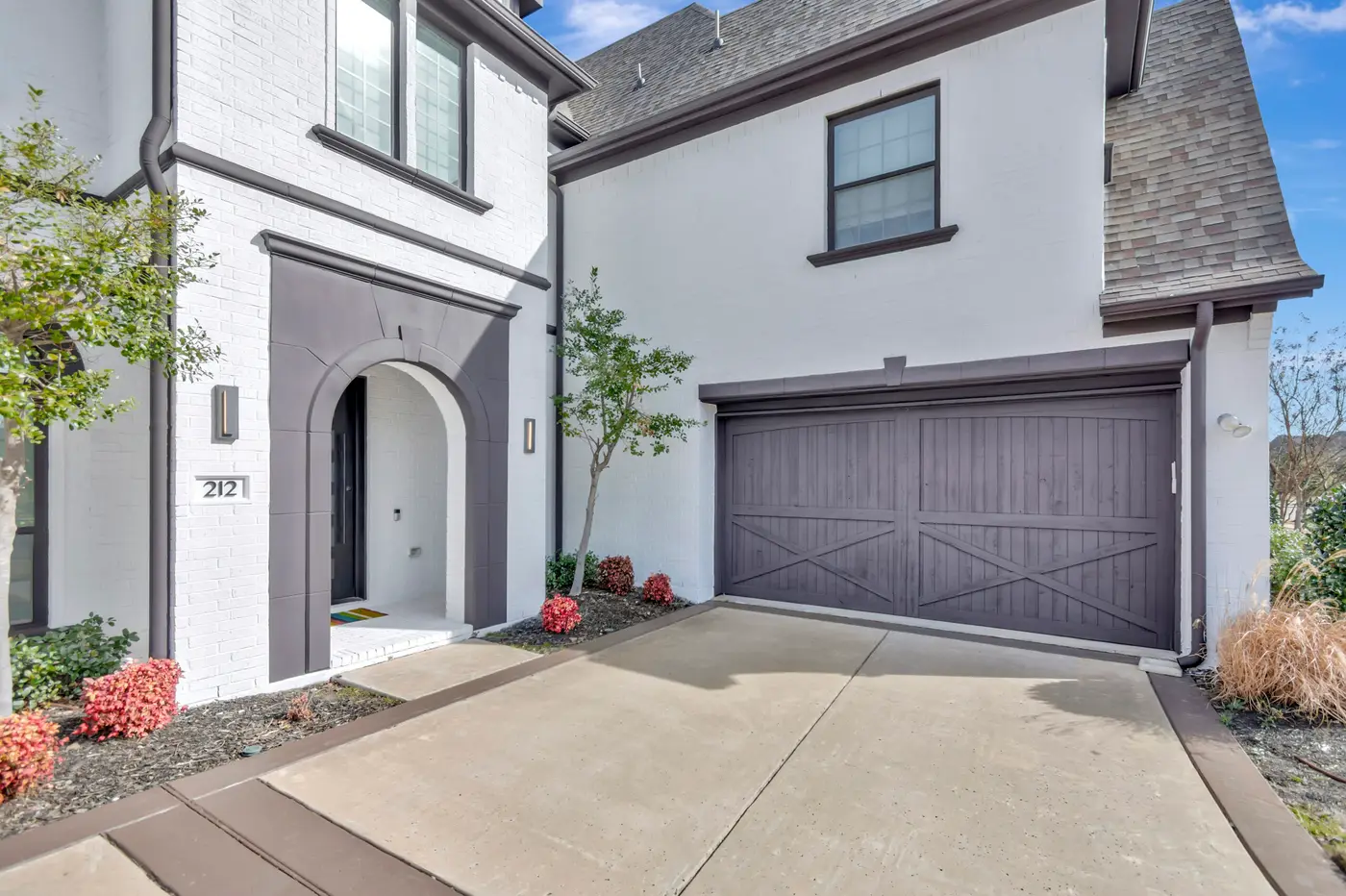 Arched entry surround and double carriage garage door in dark gray against white painted brick