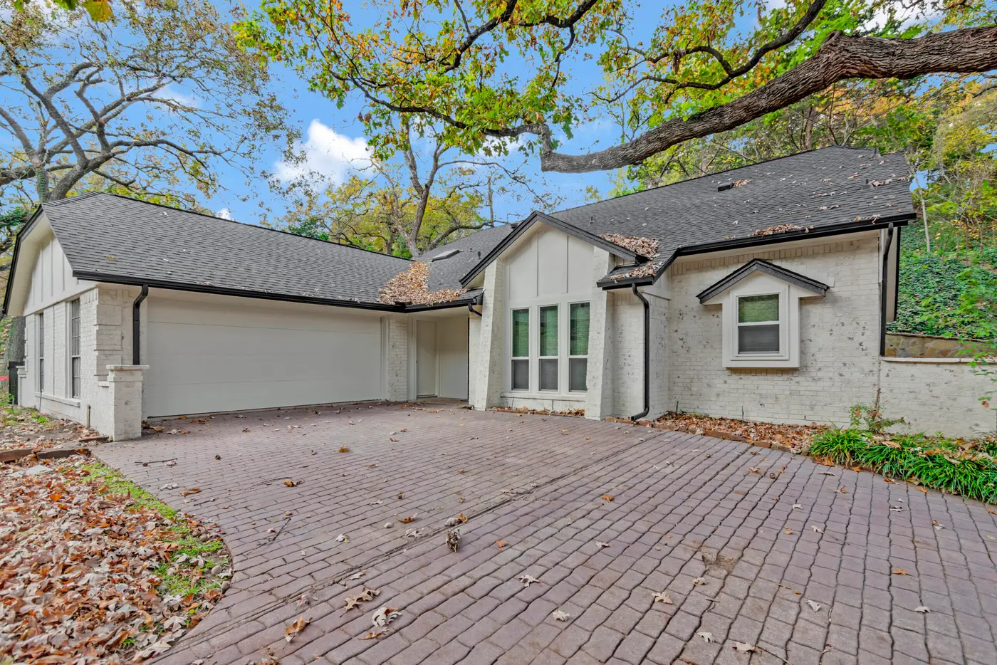 Repainted brick home with two white garage doors opening onto a brick paver forecourt