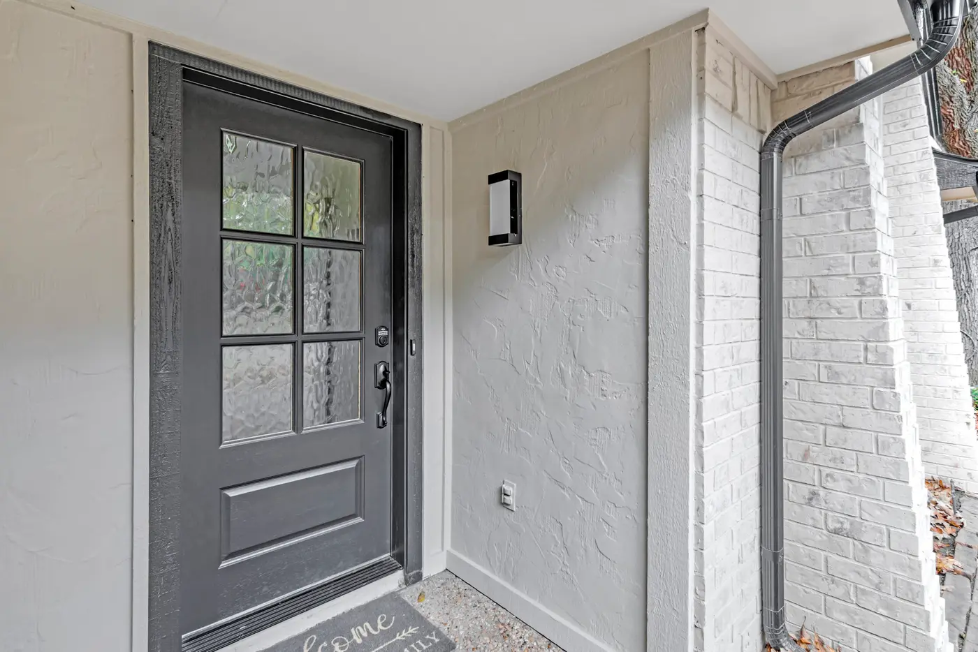 Dark gray six-pane front door set in a freshly painted entry recess with a wall lantern