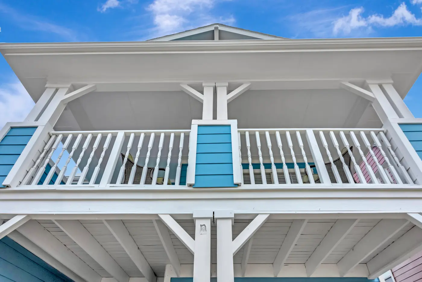 Upper balcony seen from below, with white rails and posts against blue siding