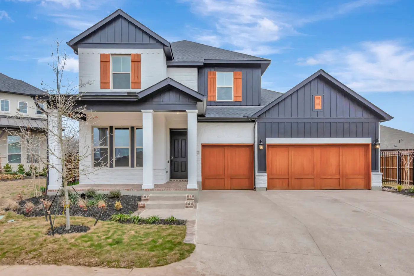 Front elevation of a modern farmhouse with white render below, dark board-and-batten above, cedar garage doors and a covered porch