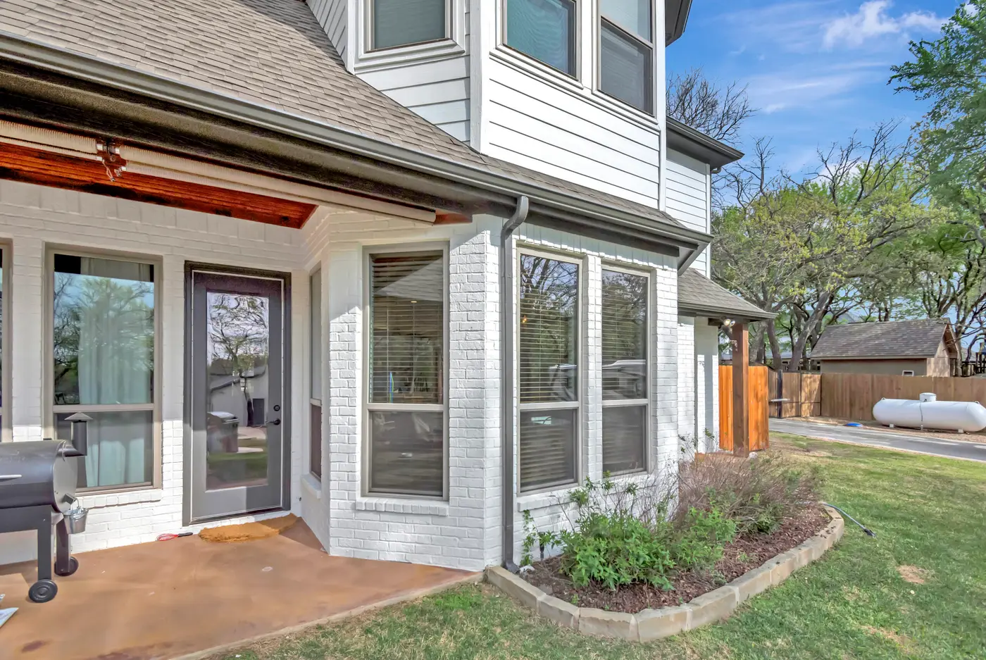 Painted brick corner with bay windows and a patio door, beside a cedar fence