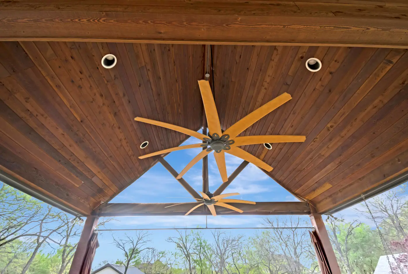 Stained cedar ceiling of a covered patio, with a large fan between recessed lights
