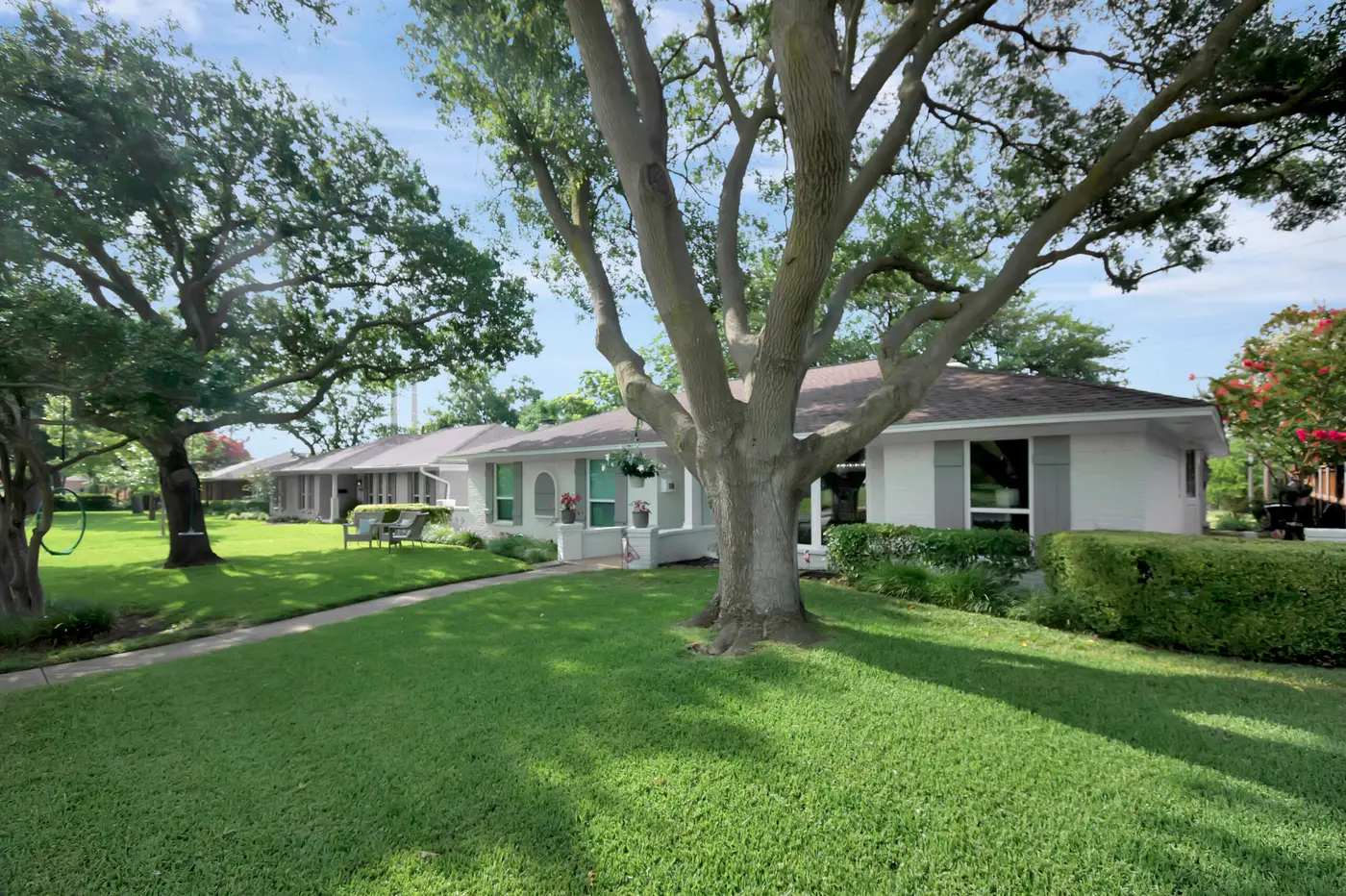 Long single-story painted home set back behind a deep lawn and mature live oaks