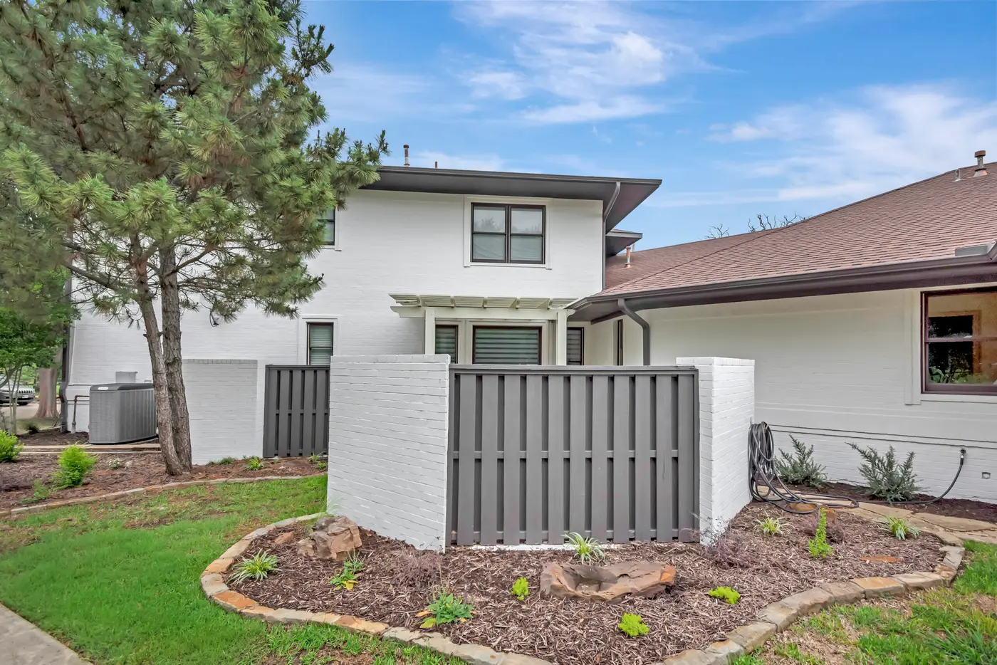 Side return of a white painted house with a gray screen fence and planted border
