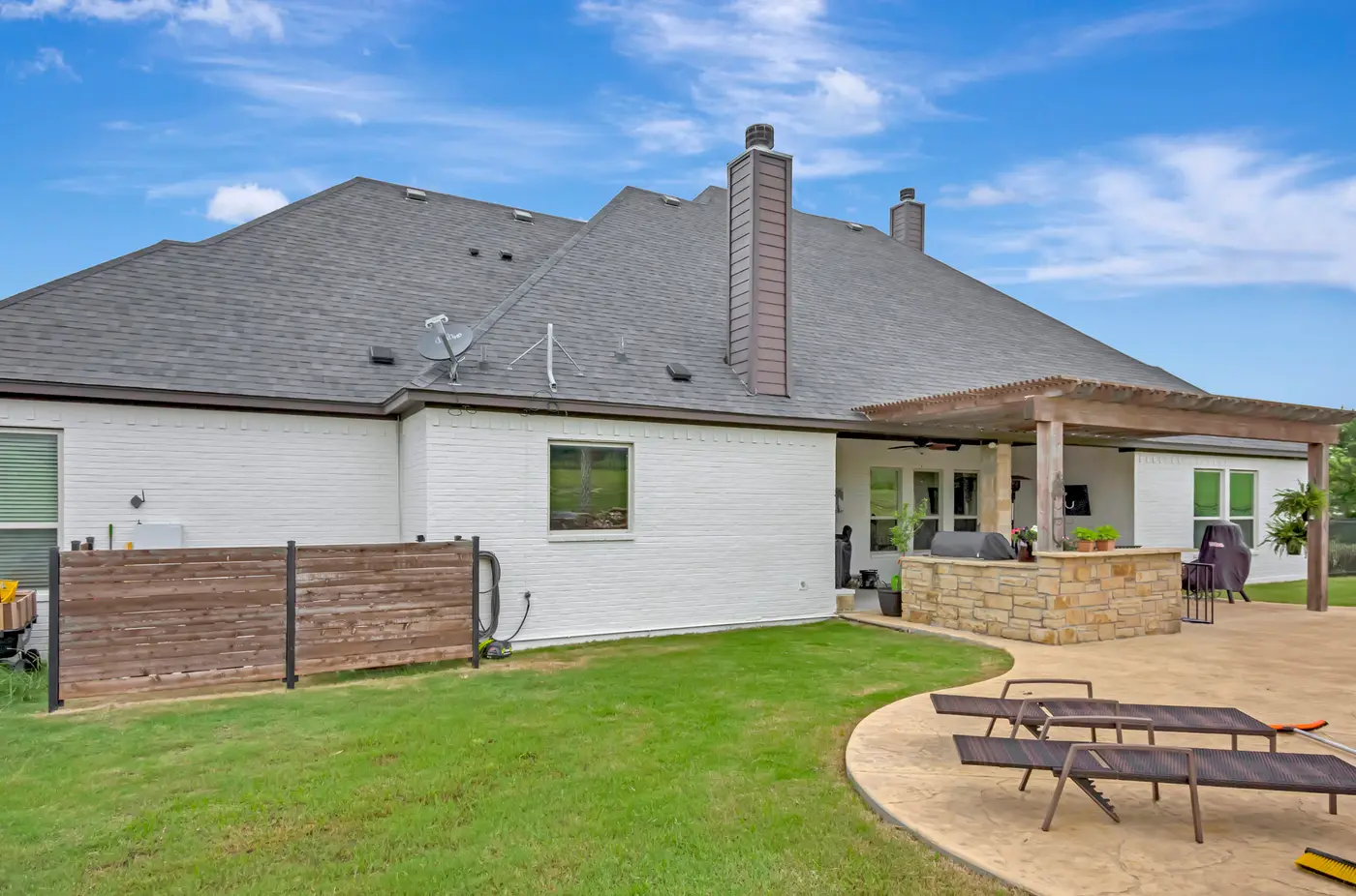 Rear elevation in painted brick with a chimney, timber screen and a pergola over the patio
