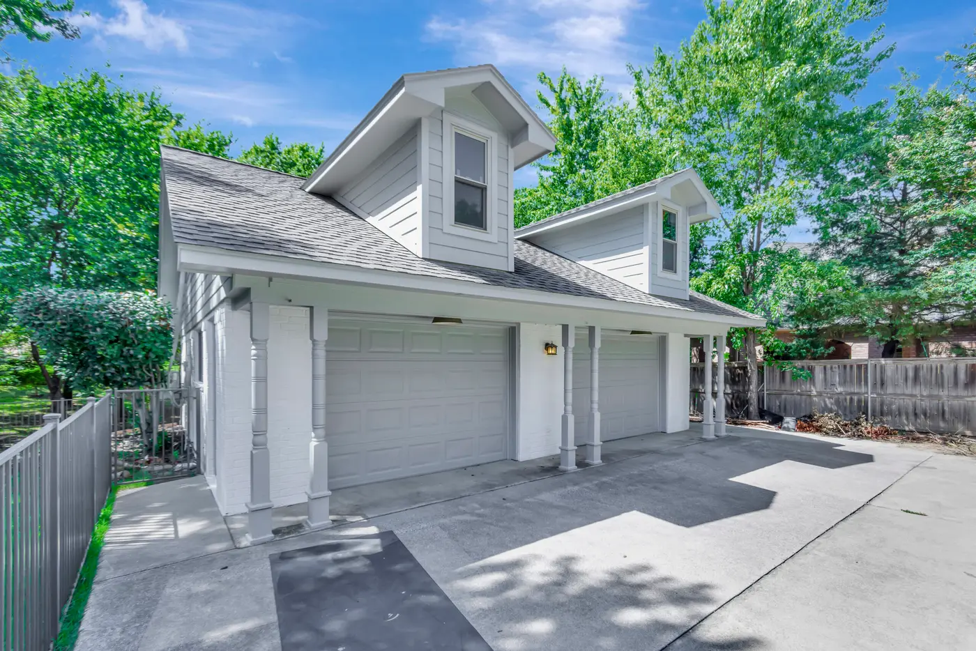 Detached painted garage with two white doors, dormers above and a timber fence beside