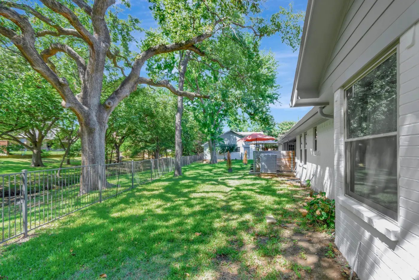 Side lawn beside a painted elevation, looking toward a shaded patio under oaks