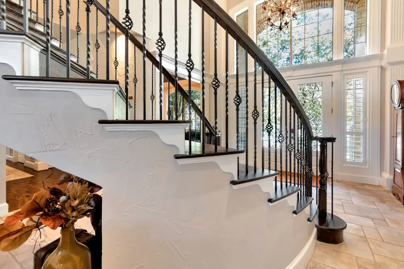 Curved staircase with a painted stringer and dark iron balusters below an arched window