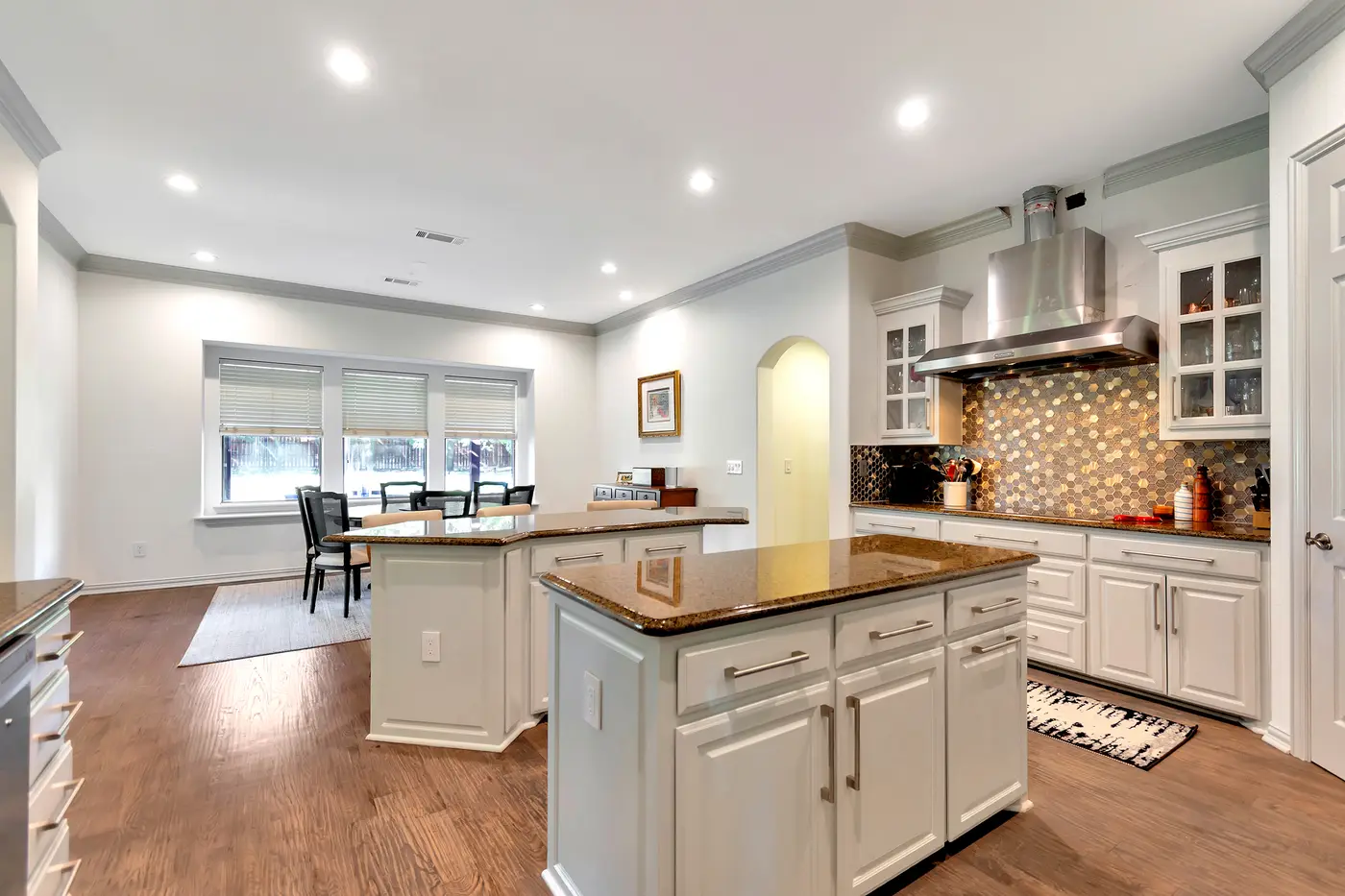 Kitchen with two painted islands, an range hood and a mosaic backsplash