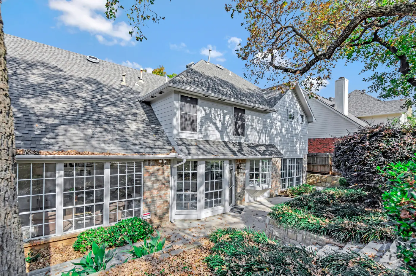 Rear elevation of a two-story home in painted brick and shingle, with banked planting
