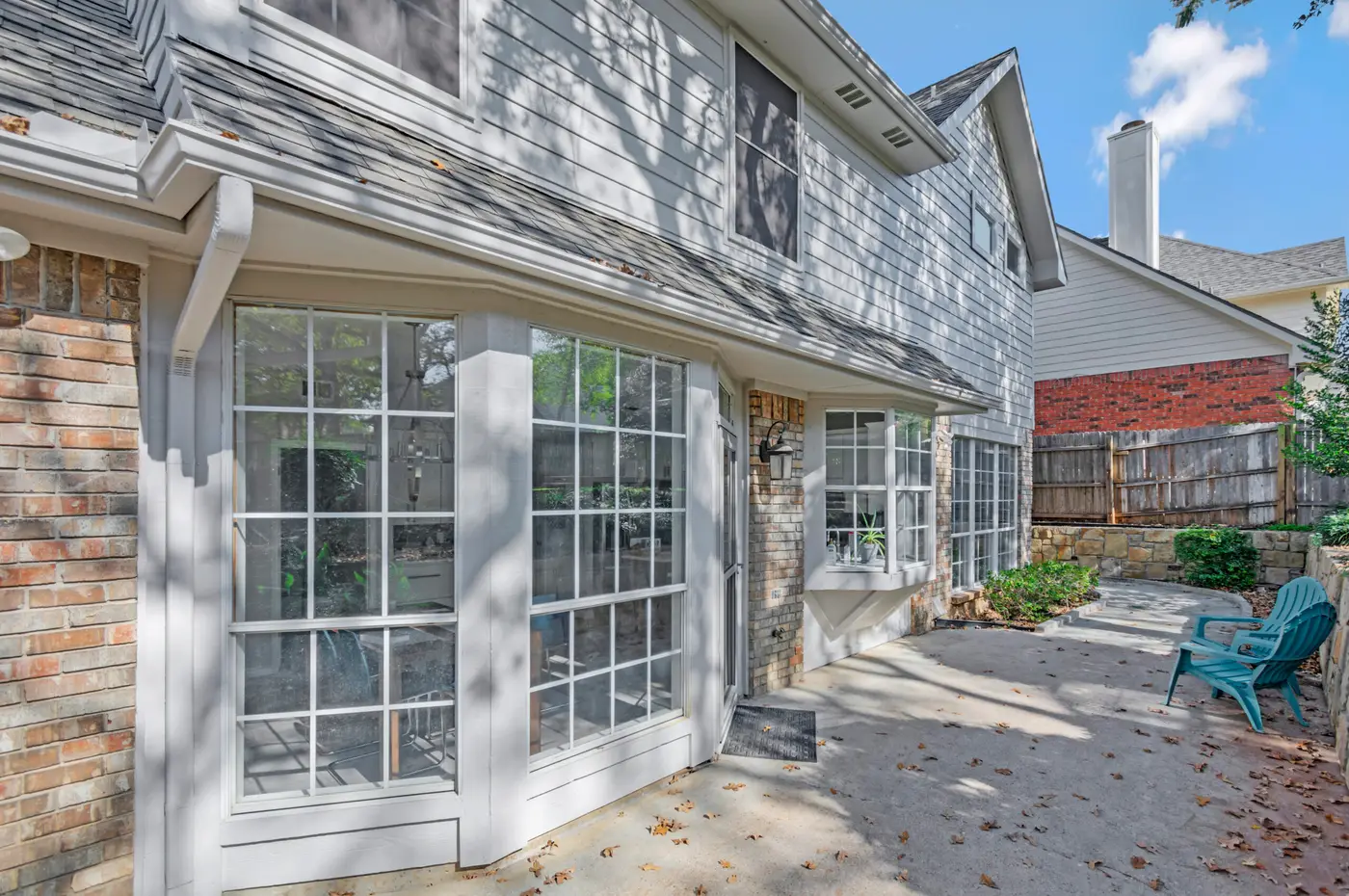 Painted bay window and trim against brick and shingle, beside a paved rear terrace