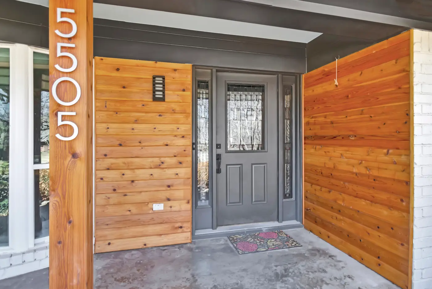 Entry porch with stained cedar cladding either side of a dark glazed front door