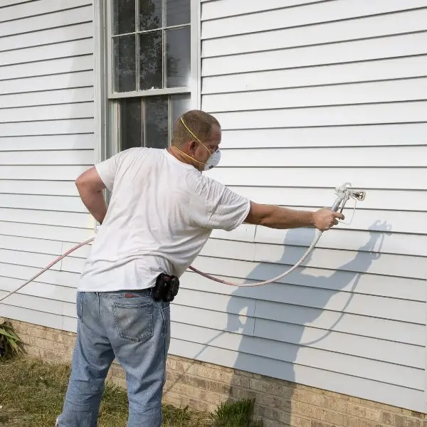 man spraying siding of house with paint