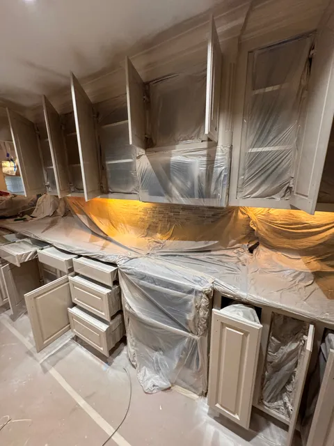 A kitchen cabinet run with the doors removed and the boxes and countertop masked off, ready for refinishing