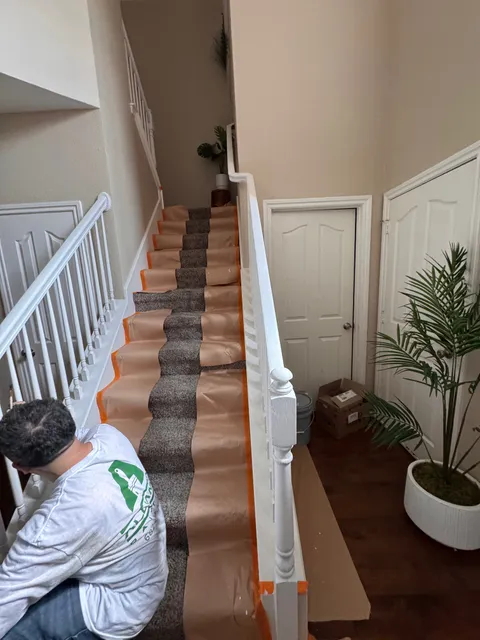 A team member taping protective paper over a carpeted staircase and its white balusters
