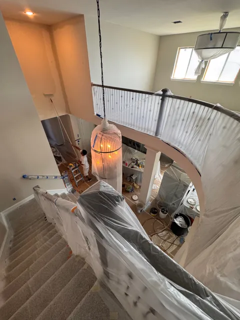 A curved staircase and upstairs landing wrapped in plastic sheeting, the pendant light bagged, before any painting starts