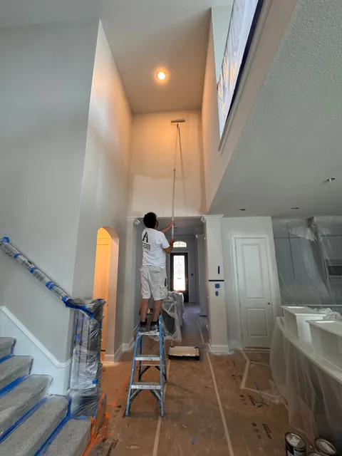 A painter working from a step ladder in a two-story stairwell, the stairs sheeted and the floor covered in rosin paper
