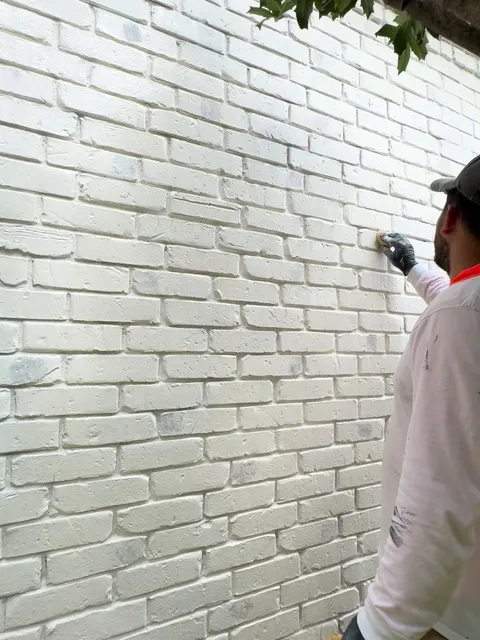 A painter working coating into a large white-painted brick elevation by hand