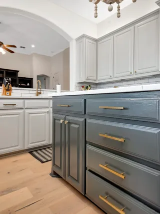 Kitchen island painted a deep gray with brass hardware, against white perimeter cabinets