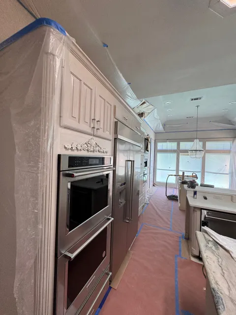 Refinished cream cabinetry around a stainless wall oven, the floor still papered and taped